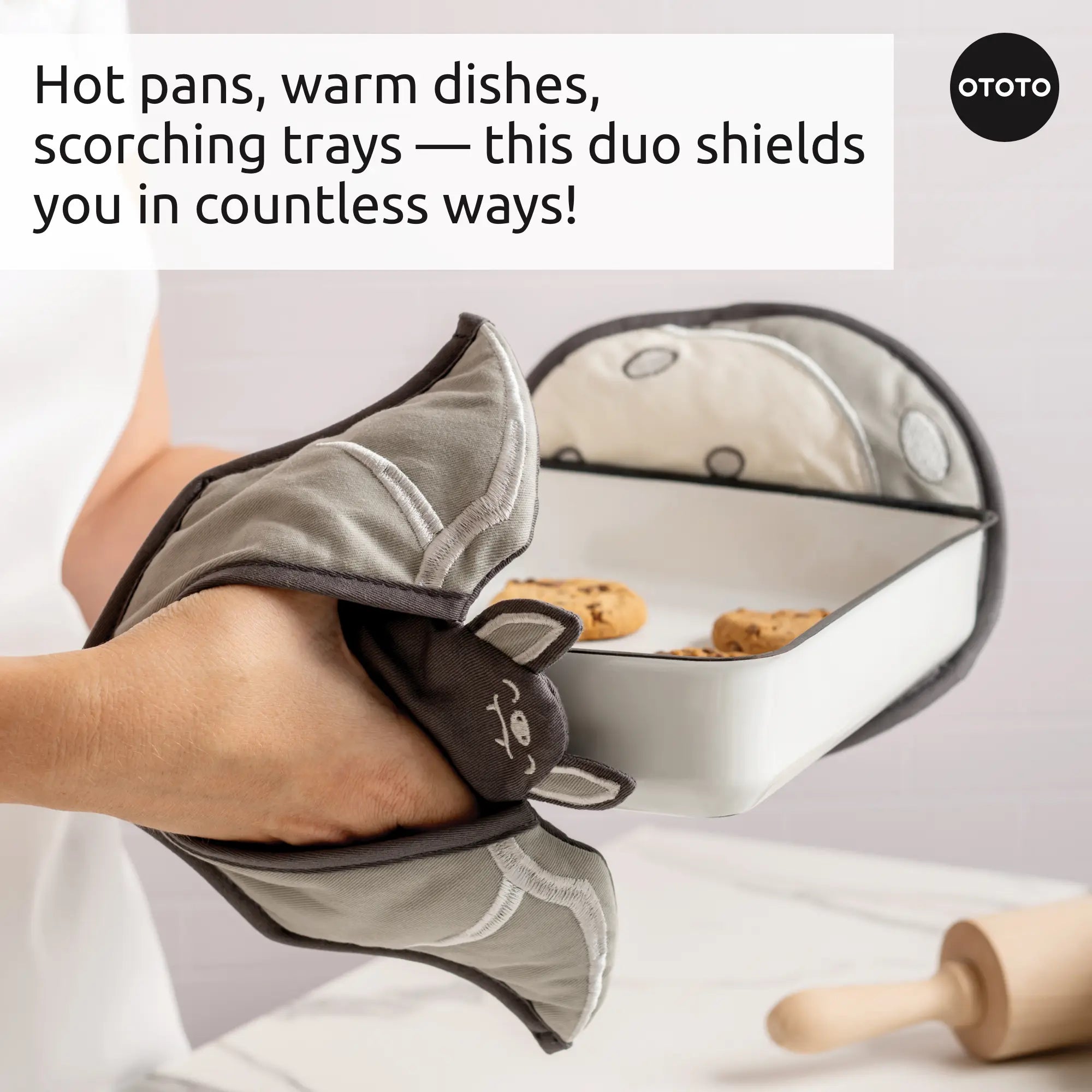 A person uses Batlicious cute animal-shaped oven mitts to hold a hot baking dish of cookies.