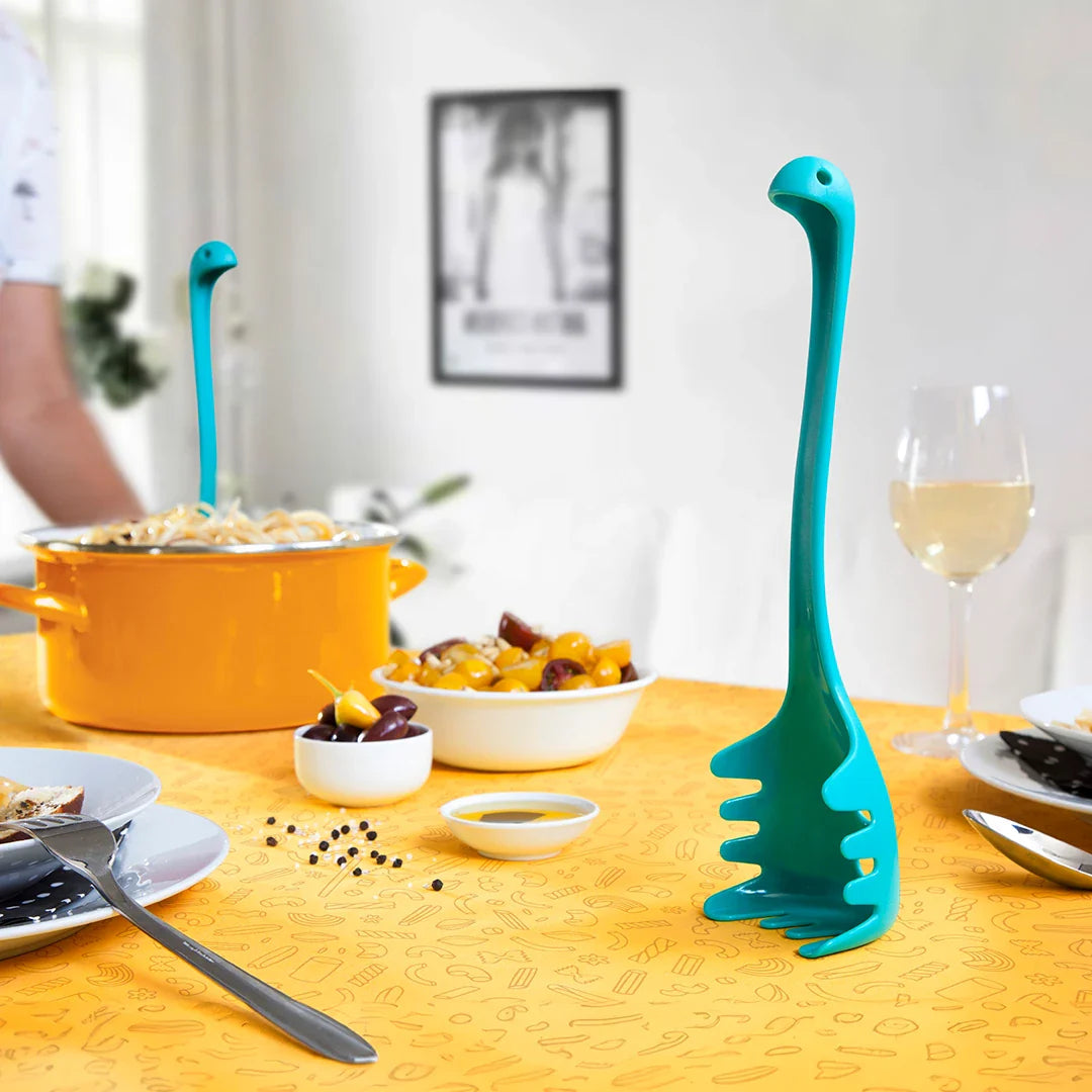 Papa Nessie, a blue dinosaur-shaped pasta spoon by OTOTO, sits beside a pot on the dining table.