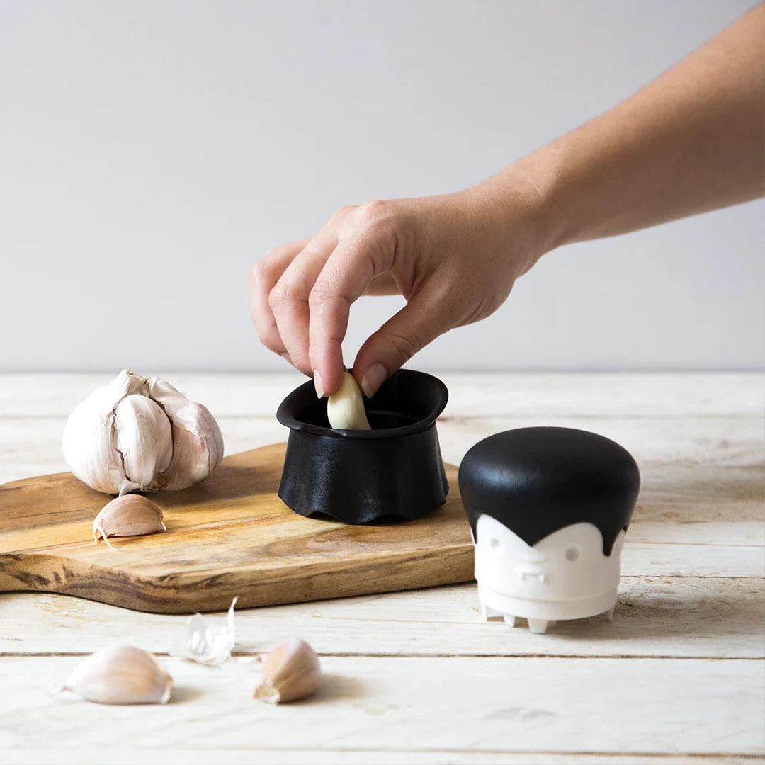 Hand using the Gracula on a wooden board with garlic bulbs.