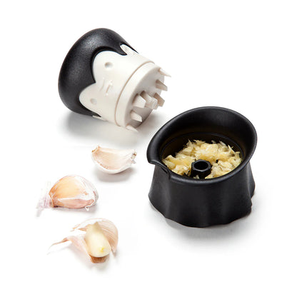 Gracula garlic crusher, featuring a black and white bat design, sits beside peeled and crushed cloves.