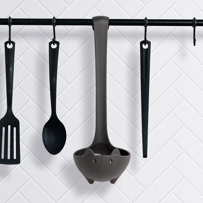OTOTOs Katie soup ladle, spatula, spoon, and tongs hang on hooks against a white tiled wall.