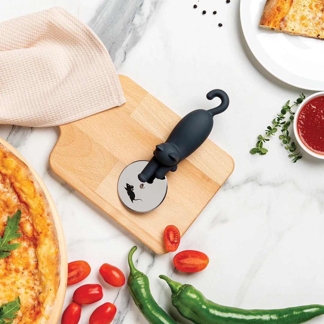 Kitty-Cut pizza cutter with a cat-shaped handle on a wooden board surrounded by fresh ingredients.