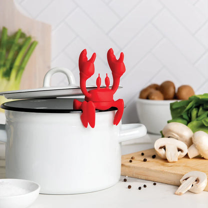 Red OTOTO utensil holder sits on a white pot, surrounded by vegetables on a cutting board.