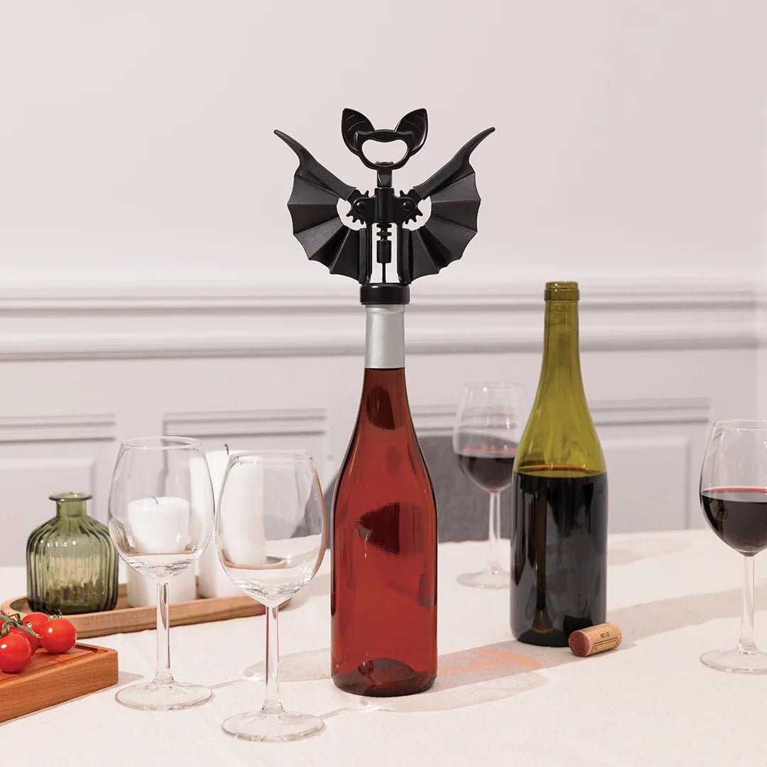 OTOTO Vino corkscrew shaped like a bat on a wine bottle, surrounded by glasses and another bottle.